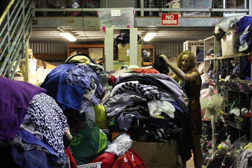A woman sorting through a room full of clothing and household products.