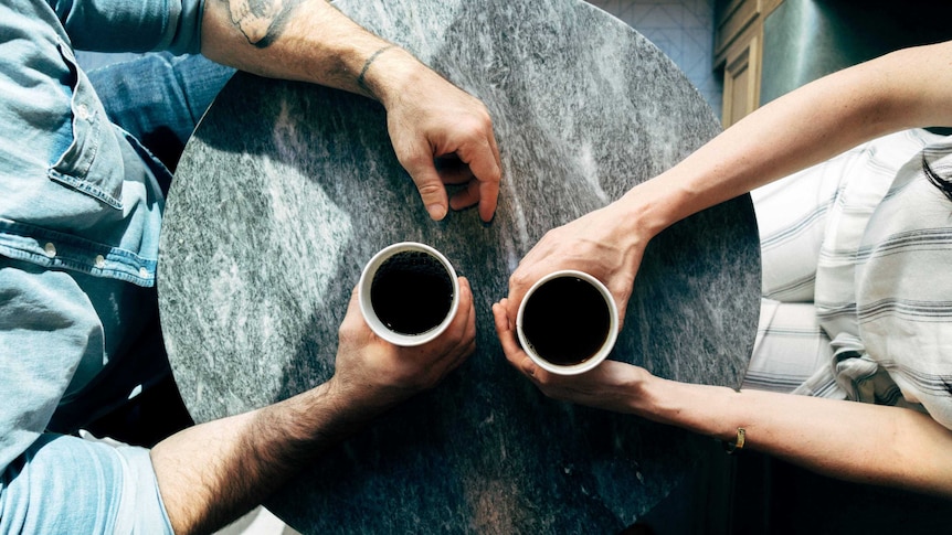 Aerial shot of couple at table holding a coffee each for a story about mental health struggles and relationships.