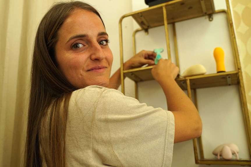 A young woman arranges sex toys on a shelf