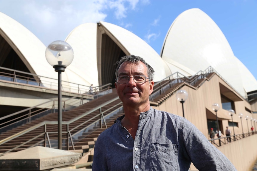 man with glasses standing near the bottom of the outside stairs of the Sydney Opera House