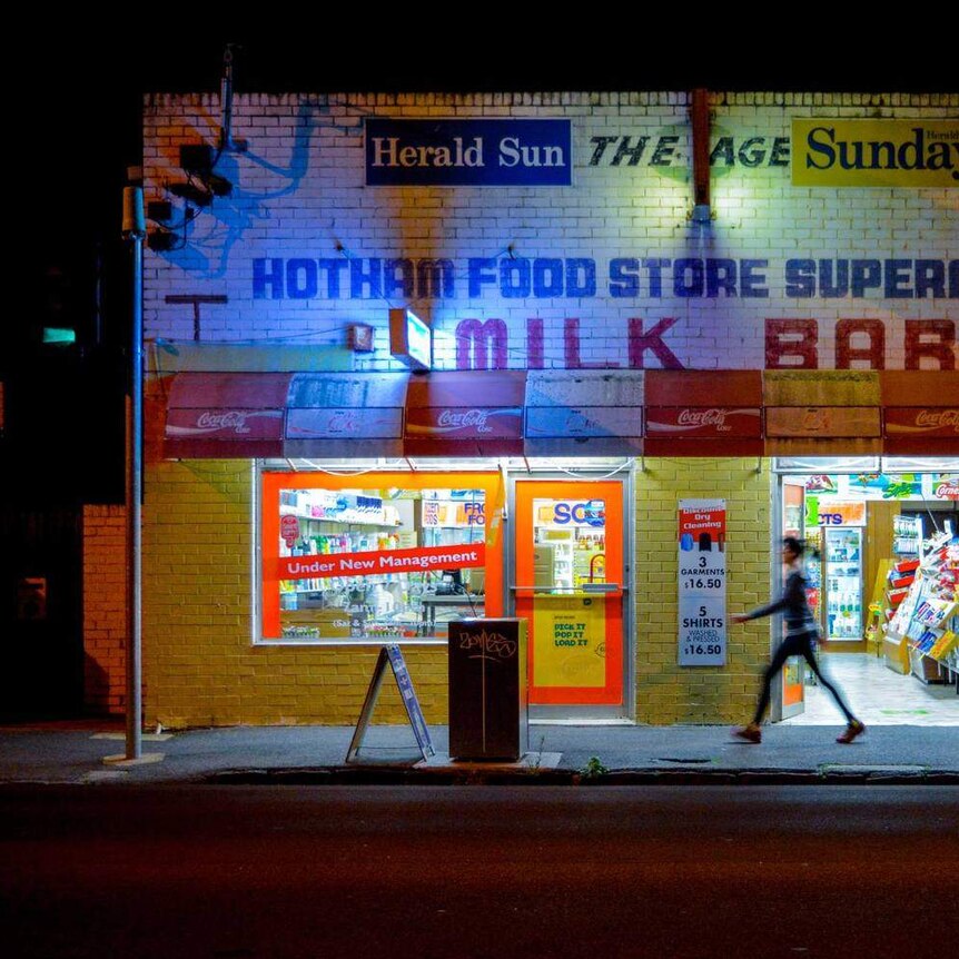 A person walks past a milk bar at night.