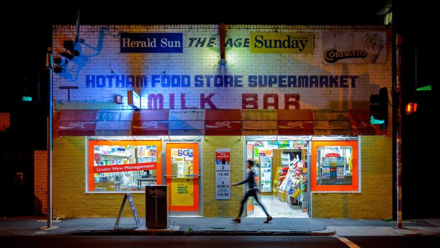 A person walks past a milk bar at night.