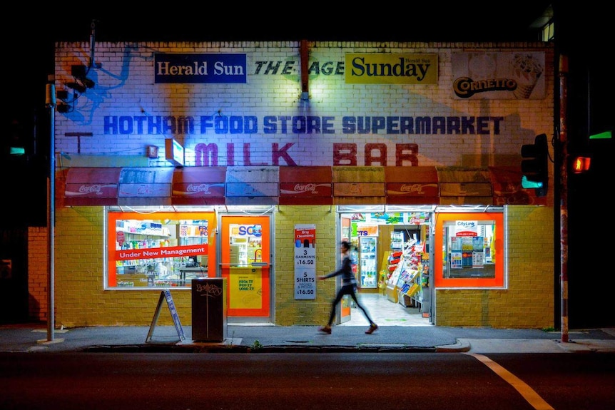 A person walks past a milk bar at night.