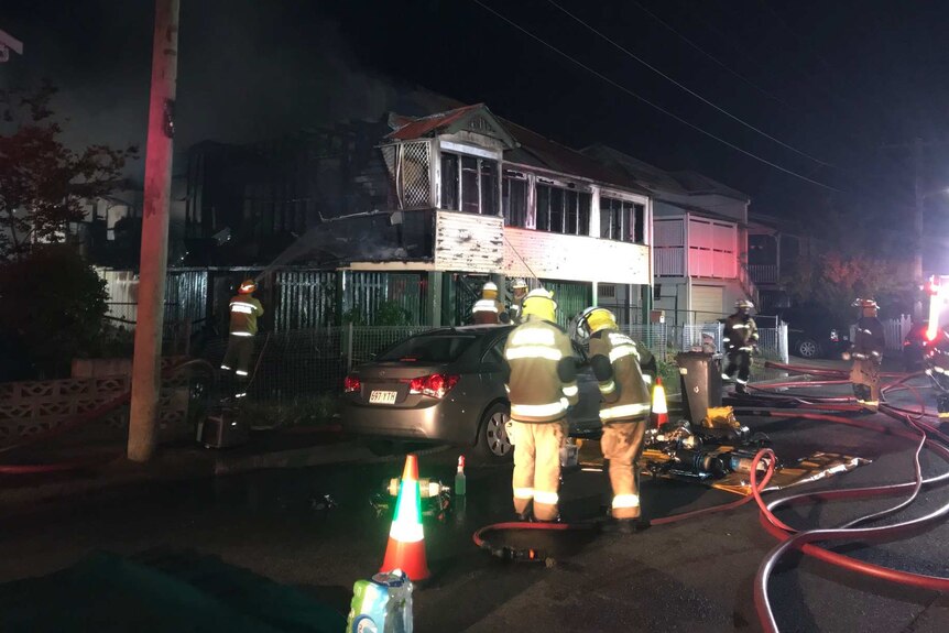 Fire crews surround a house blackened by fire at night