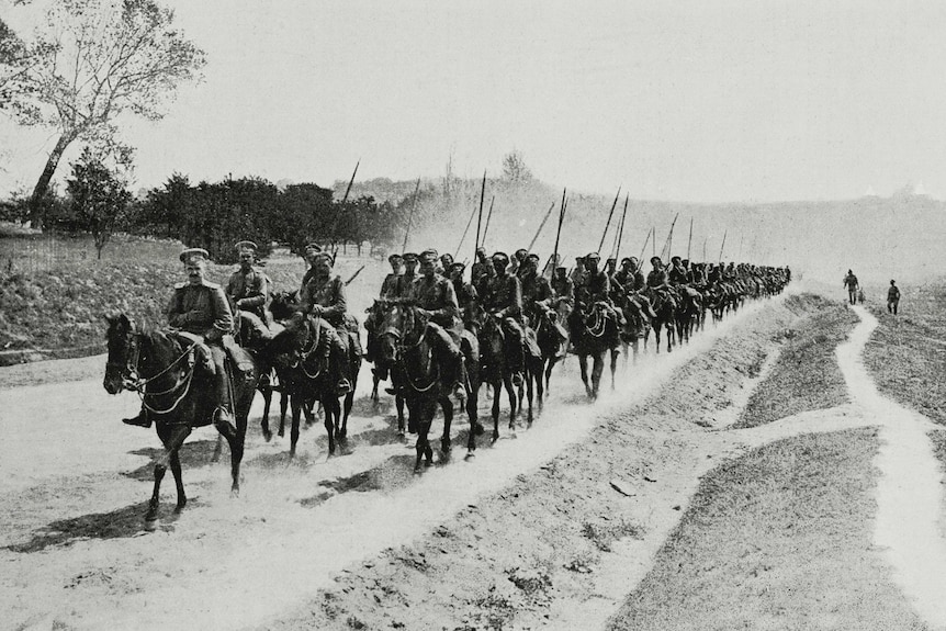 Black and white image of Russian soldiers on horse back marching down a dirt path