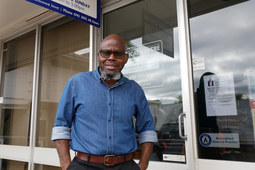 A man in a blue shirt stands in front of a medical centre.