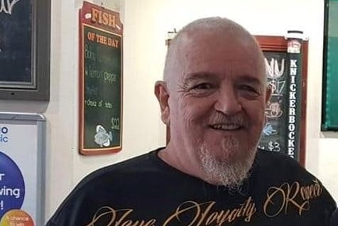 An older, heavyset man stands smiling in what appears to be a bistro.