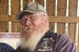 A man with a beard, cap, and glasses, wearing a Dartmoor Angling Club shirt