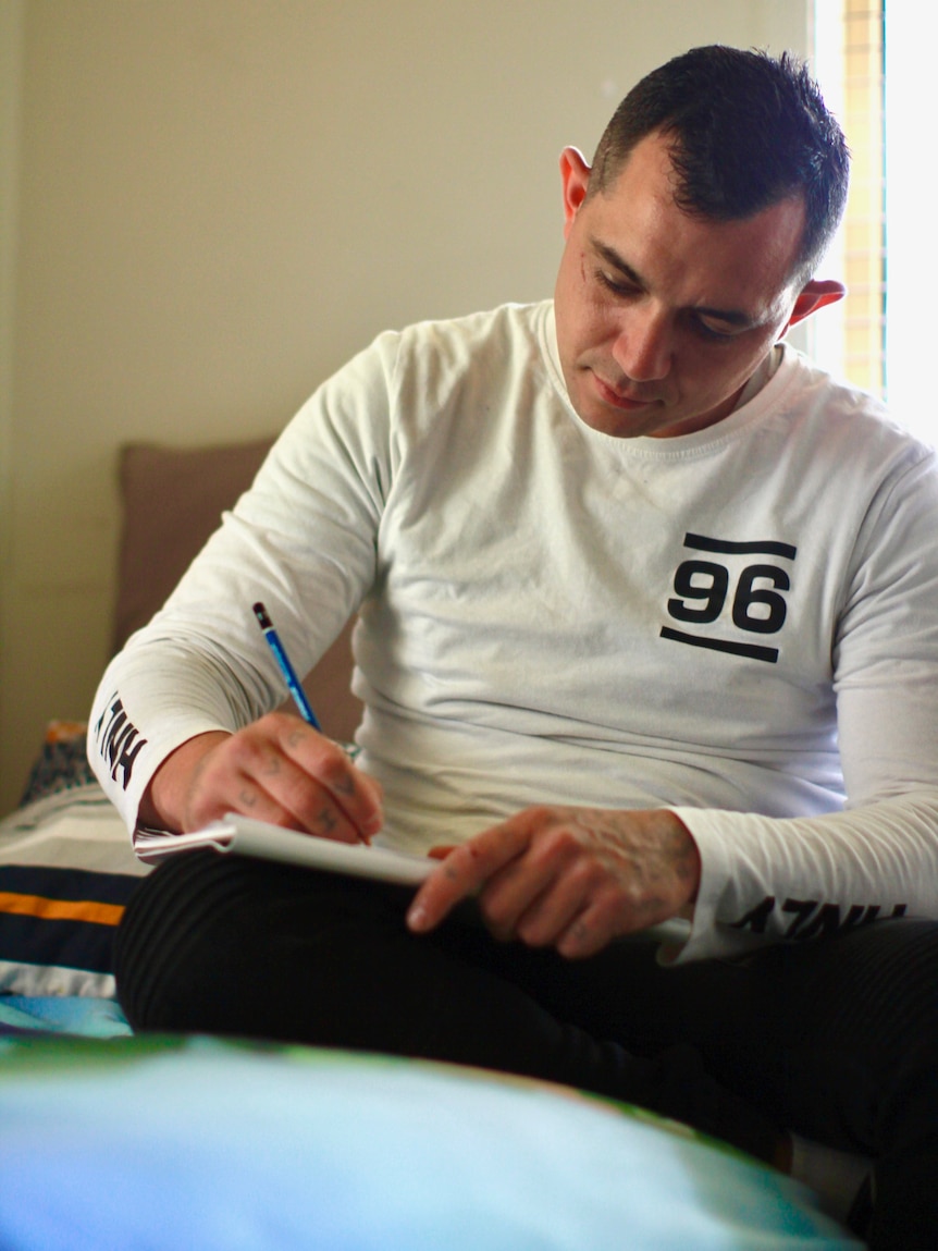 Man in long white shirt writing in notebook.