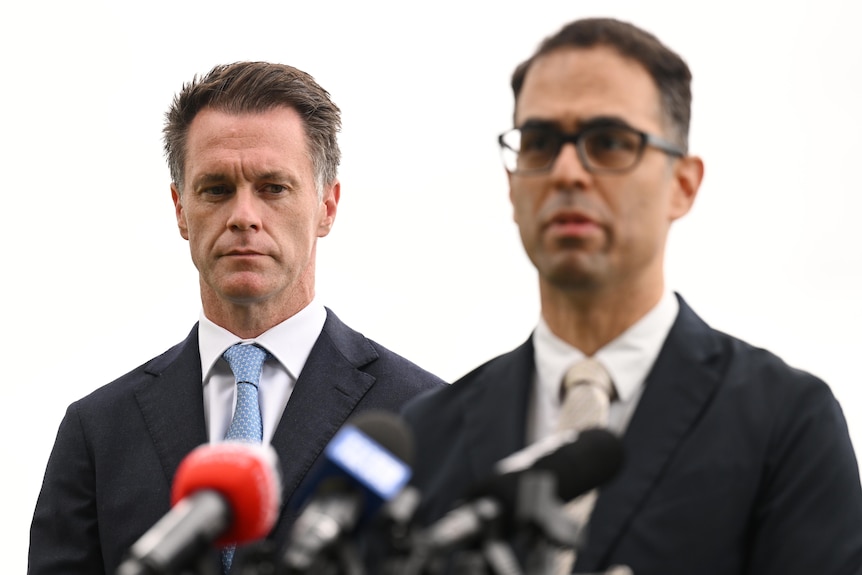 two men talking to the media, one is wearing glasses