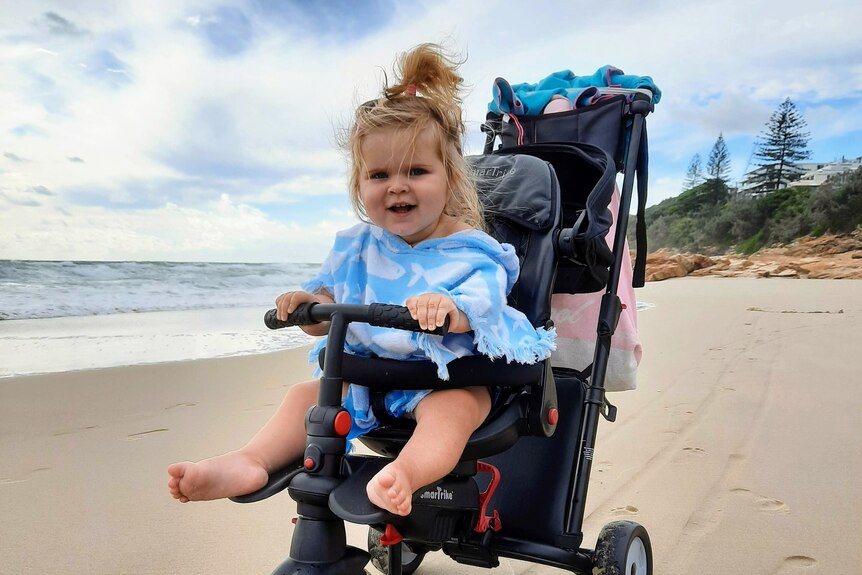 Baby sitting in a pram on the beach, on a beautiful sunny day with blue sky