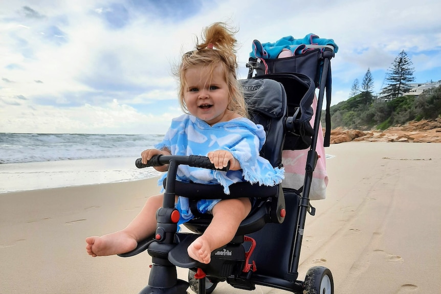 Baby sitting in a pram on the beach, on a beautiful sunny day with blue sky
