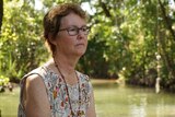 A woman wearing a mournful look sits facing a creek in Darwin. 