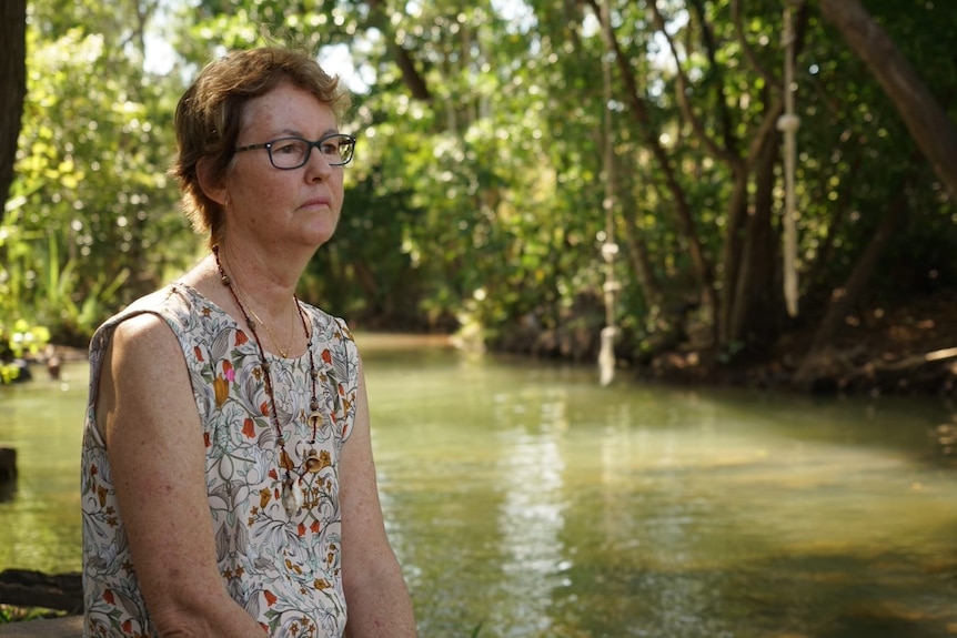 Une femme au regard triste est assise face à une crique de Darwin. 