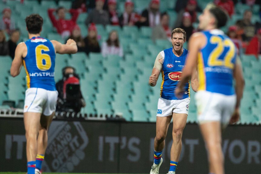 An AFL player roars in celebration of a goal, while one of his teammates holds out his fist to bump.