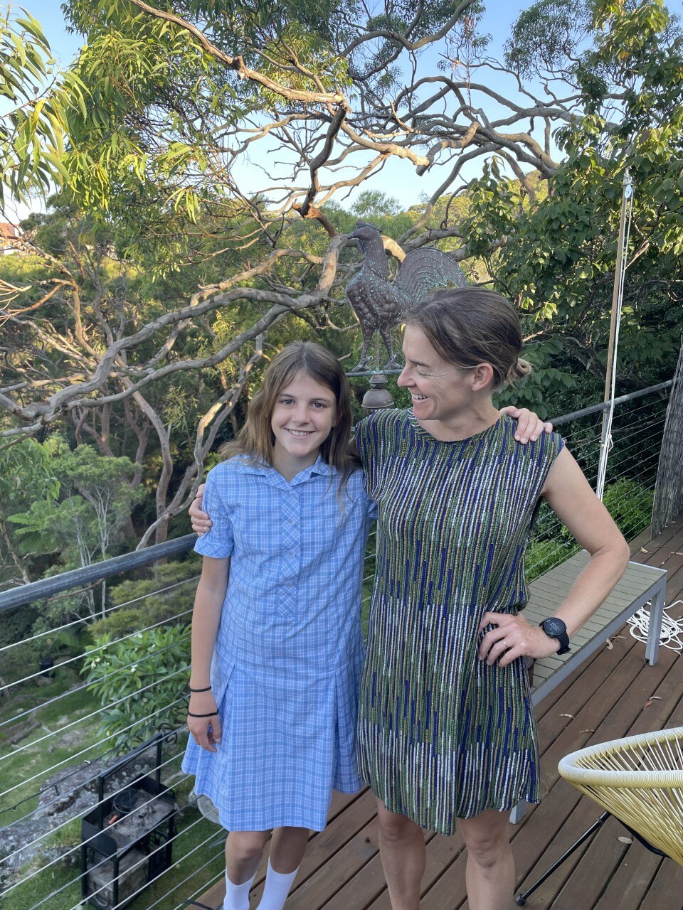 A woman stands proudly beside her school-aged daughter who is wearing a school uniform.