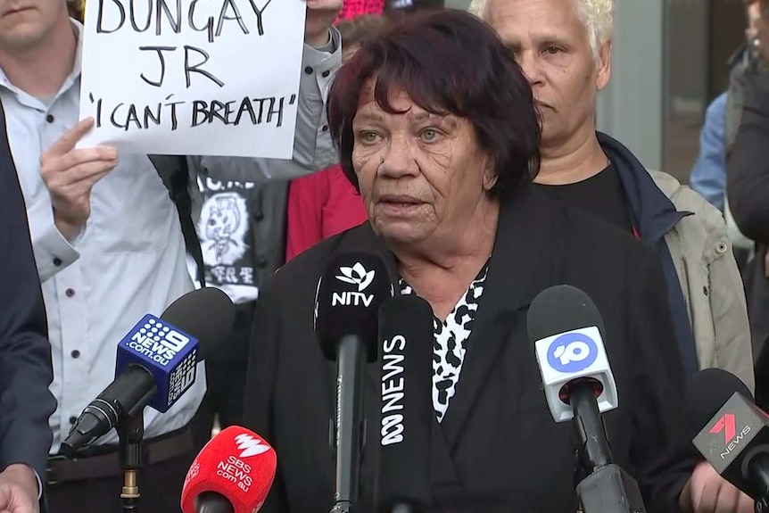 A woman stands in front of microphones.