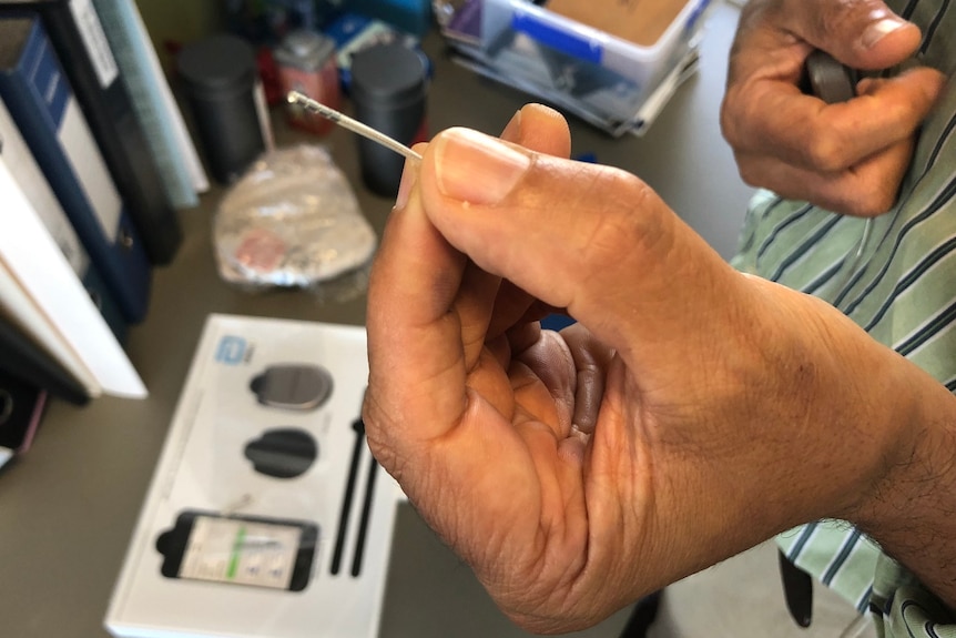 A man's hand holds a small electrode to be  implanted in the brain.