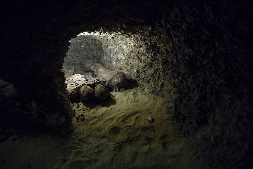 Three mummies wrapped in linen seen in a rocky hollow of a chamber