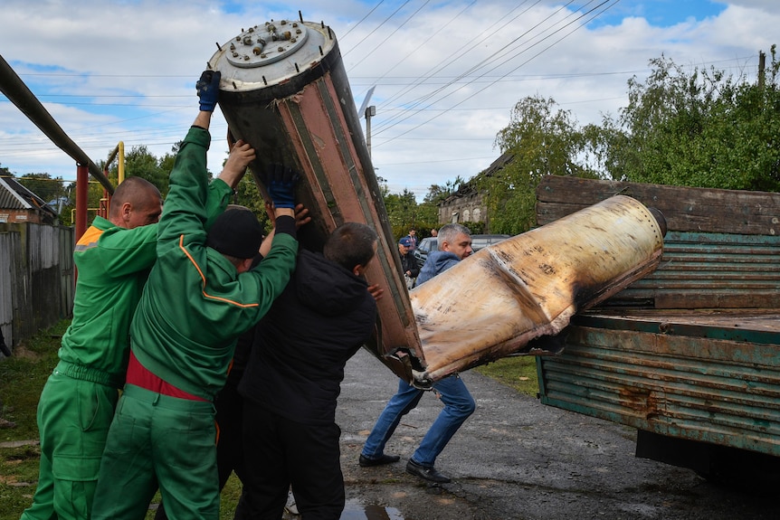 Communal workers load remains of a missile into a truck.