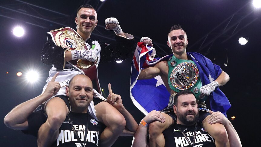 Jason and Andrew Moloney sit on their trainers shoulders and smile with boxing belts