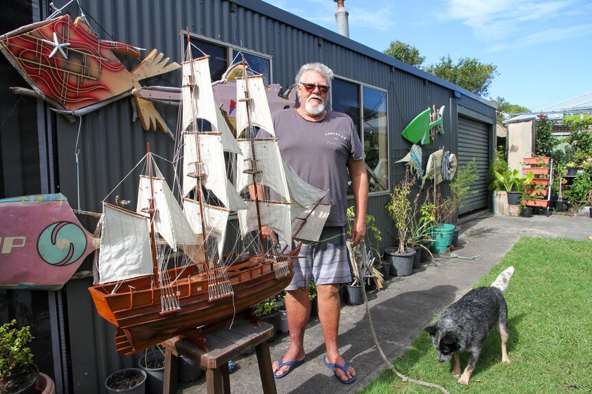 A man and his dog stand next to a model tall ship.