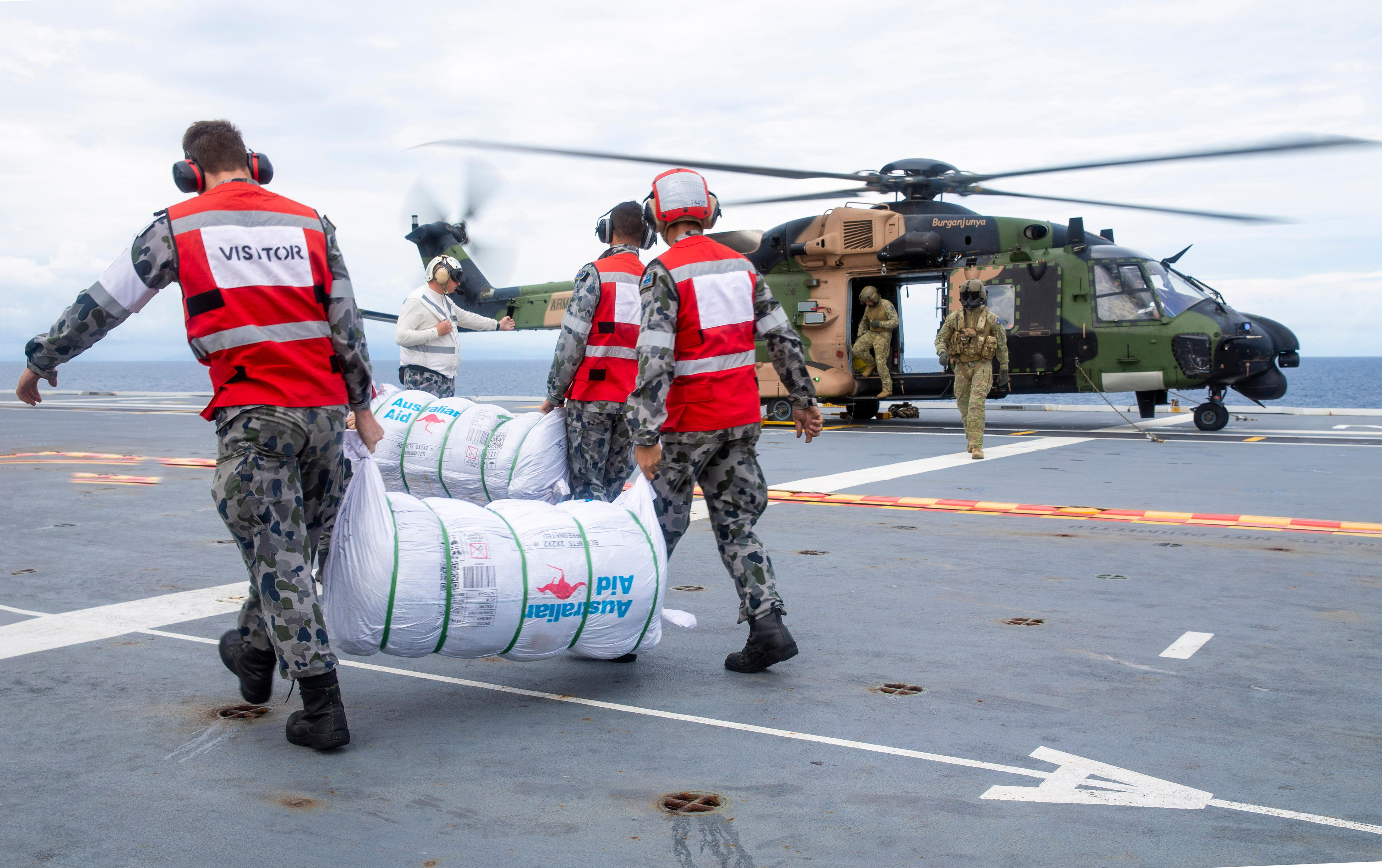 Defence personnel carry large bundles of aid towards a helicopter that's parked on a navy vessel.
