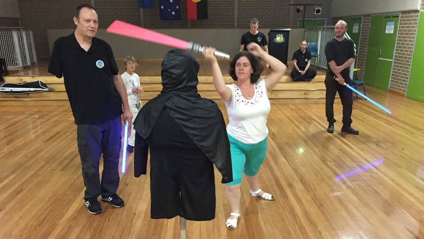 A woman with a red lightsaber takes a swipe at a dummy dressed in black