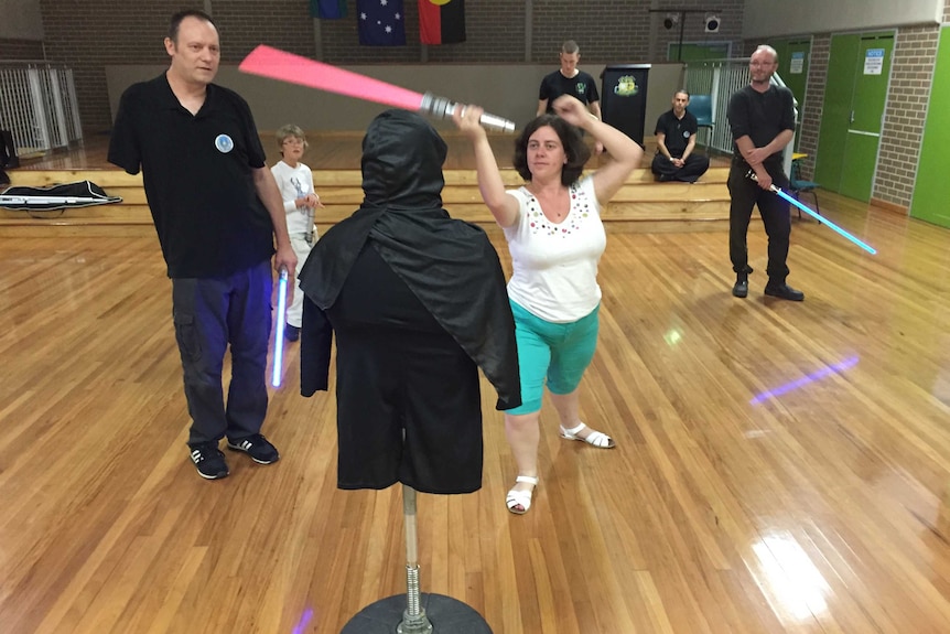 A woman with a red lightsaber takes a swipe at a dummy dressed in black