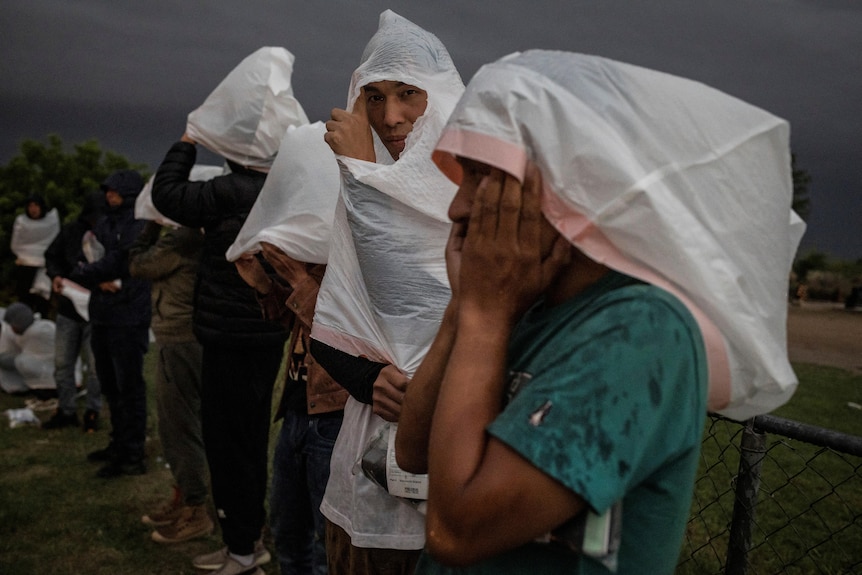 Chinese migrants wear rubbish bags over their heads to keep the rain out after arriving in Texas.