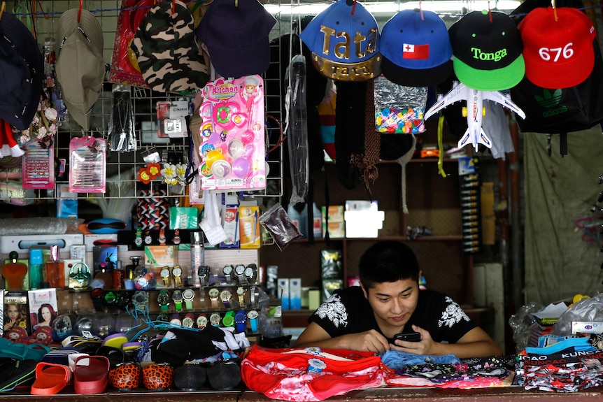 A young person looks at their phone in a stall with caps and other goods.