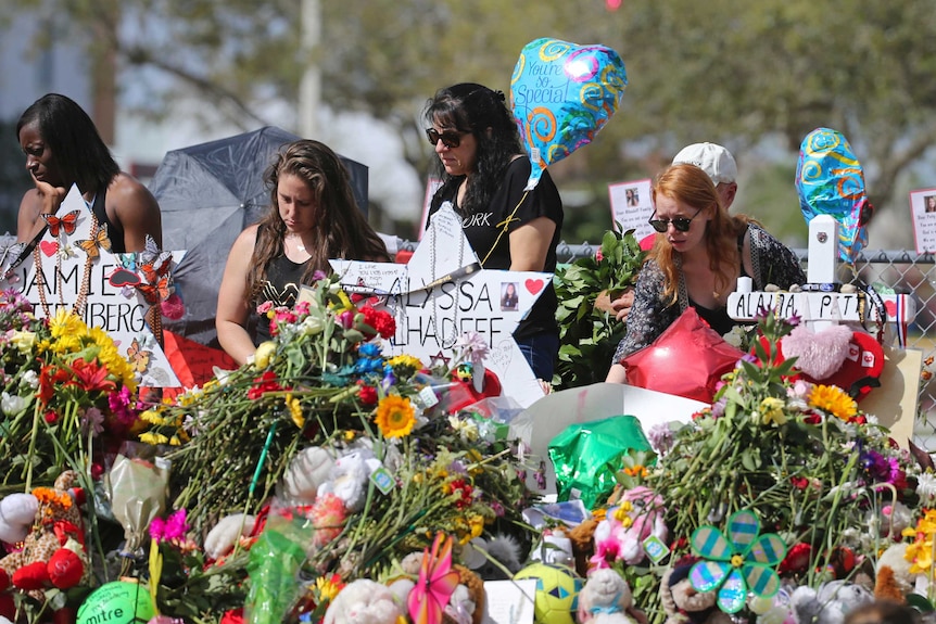 Mourners pay tribute at a school shooting memorial covered with flowers.