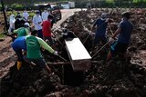 Workers lower a coffin into a grave surrounded by mud