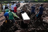 Workers lower a coffin into a grave surrounded by mud
