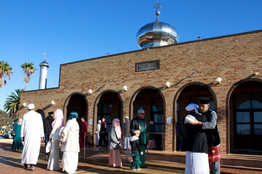 People gather outside mosque on sunny day