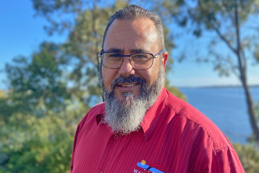 A man with a beard wearing a red top looks at the camera.