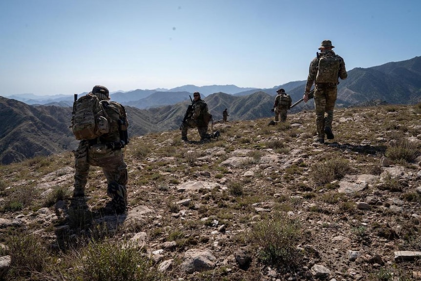 US Special Forces in combat gear on top of a mountain in Afghanistan with many mountains in the distance.