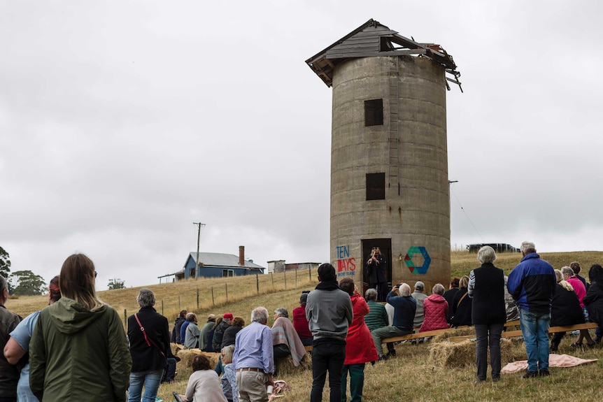 A man plays an instrument to a crowd under a tower.