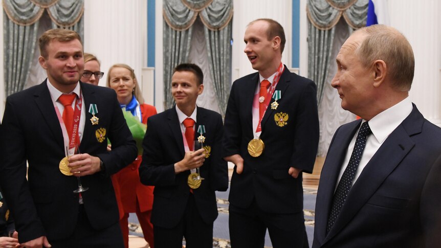 Russian President Vladimir Putin stands with Paralympians at a reception in an opulent room.