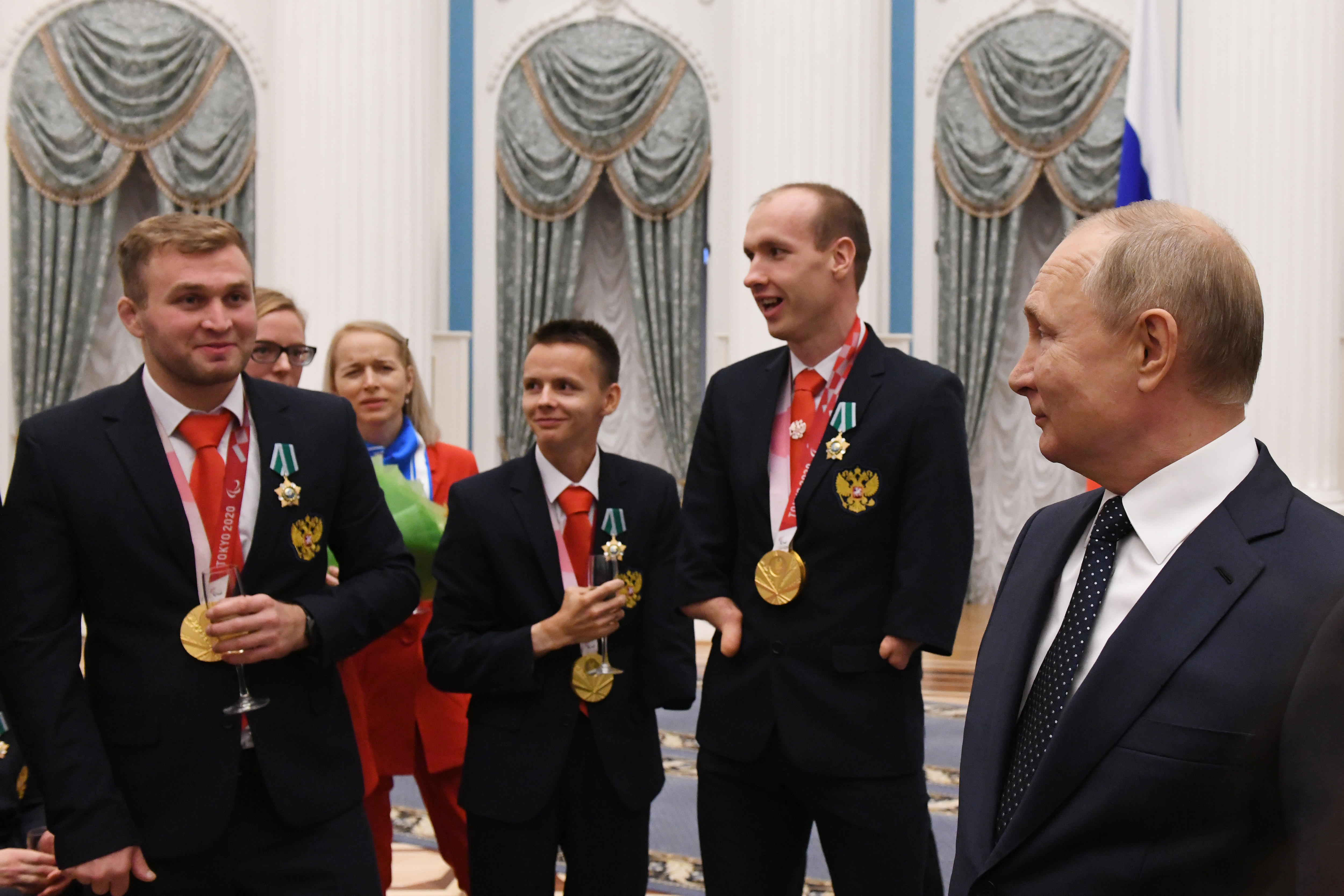 俄罗斯总统弗拉基米尔普京在招待会上与残奥会运动员站在一起在一个豪华的房间里。” class=