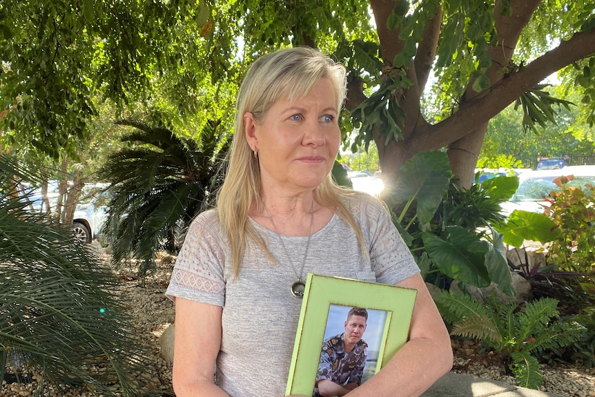 A woman stands with a photo of her son in her hands.