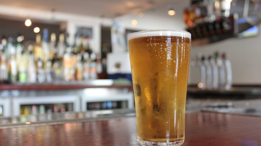 A glass of beer with drops of condensation resting on a dark wood bar.