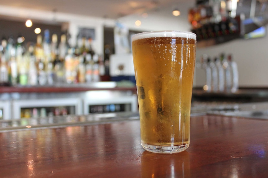 A glass of beer with drops of condensation resting on a dark wood bar.