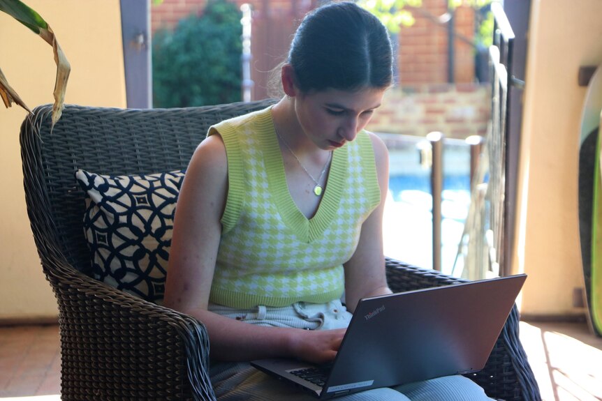April is sitting on a chair outside, looking down at her laptop screen while typing.