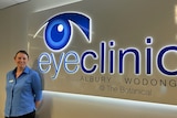An image of a middle-aged woman dressed in a blue uniform, standing in front of a sign reading 'Eye Clinic Albury-Wodonga'.