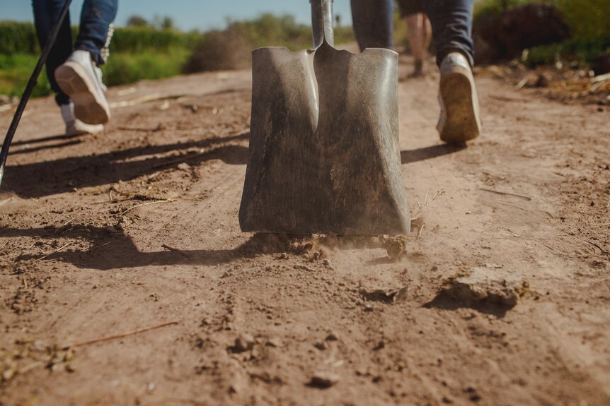 A shovel drags on the dirt road.