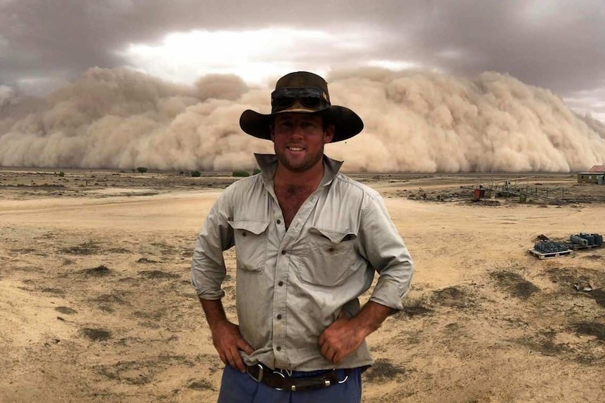 Man with hat stands in front of dust storm