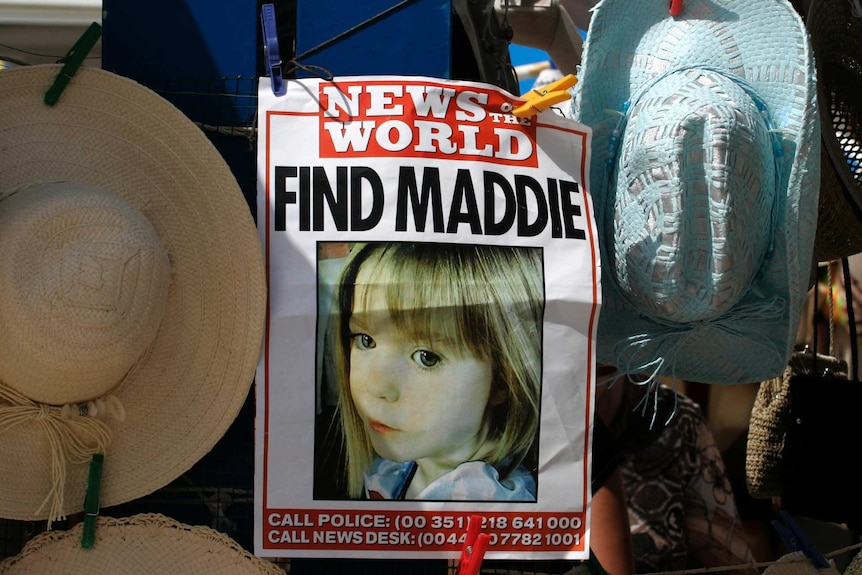 A poster of missing girl Madeleine McCann hangs between sun hats at a stall.