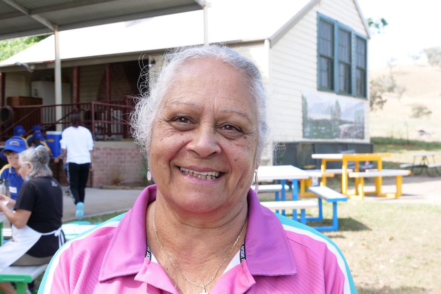 An woman  with grey hair wearing a pink shirt smiles at the camera