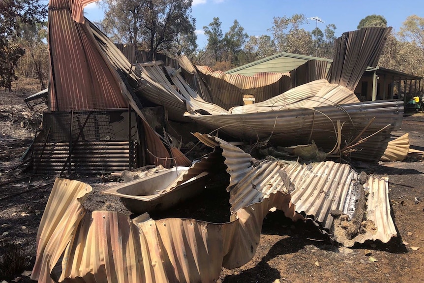 Sheets of warped and burnt corrugated iron sit on damaged belongings including a bathtub.